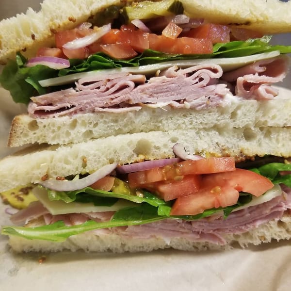 A large, sliced bagel sandwich with ham, cheese, lettuce, tomato, onion, and pickles.