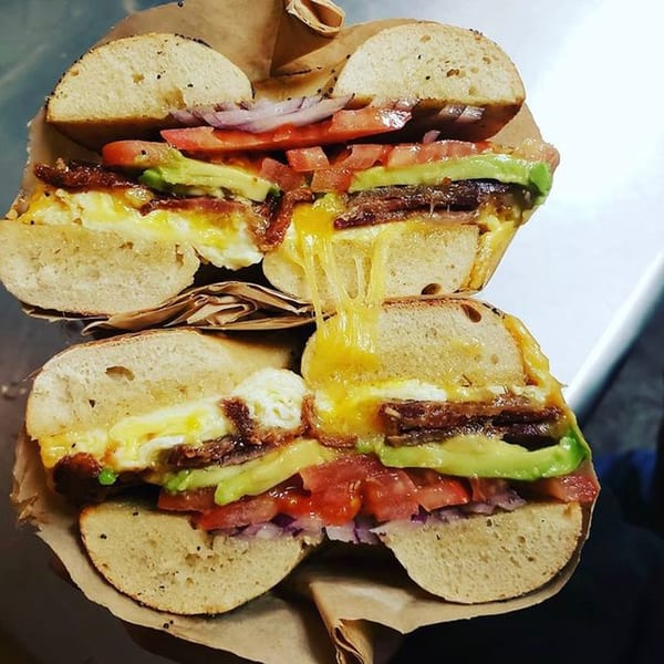 A Henry Higgins Boiled Bagels sandwich, cut in half, revealing egg, bacon, avocado, tomato, and onion.