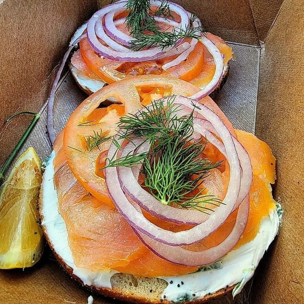 Two Henry Higgins Boiled Bagels with lox, cream cheese, red onion, tomato, and dill, with a lemon wedge.
